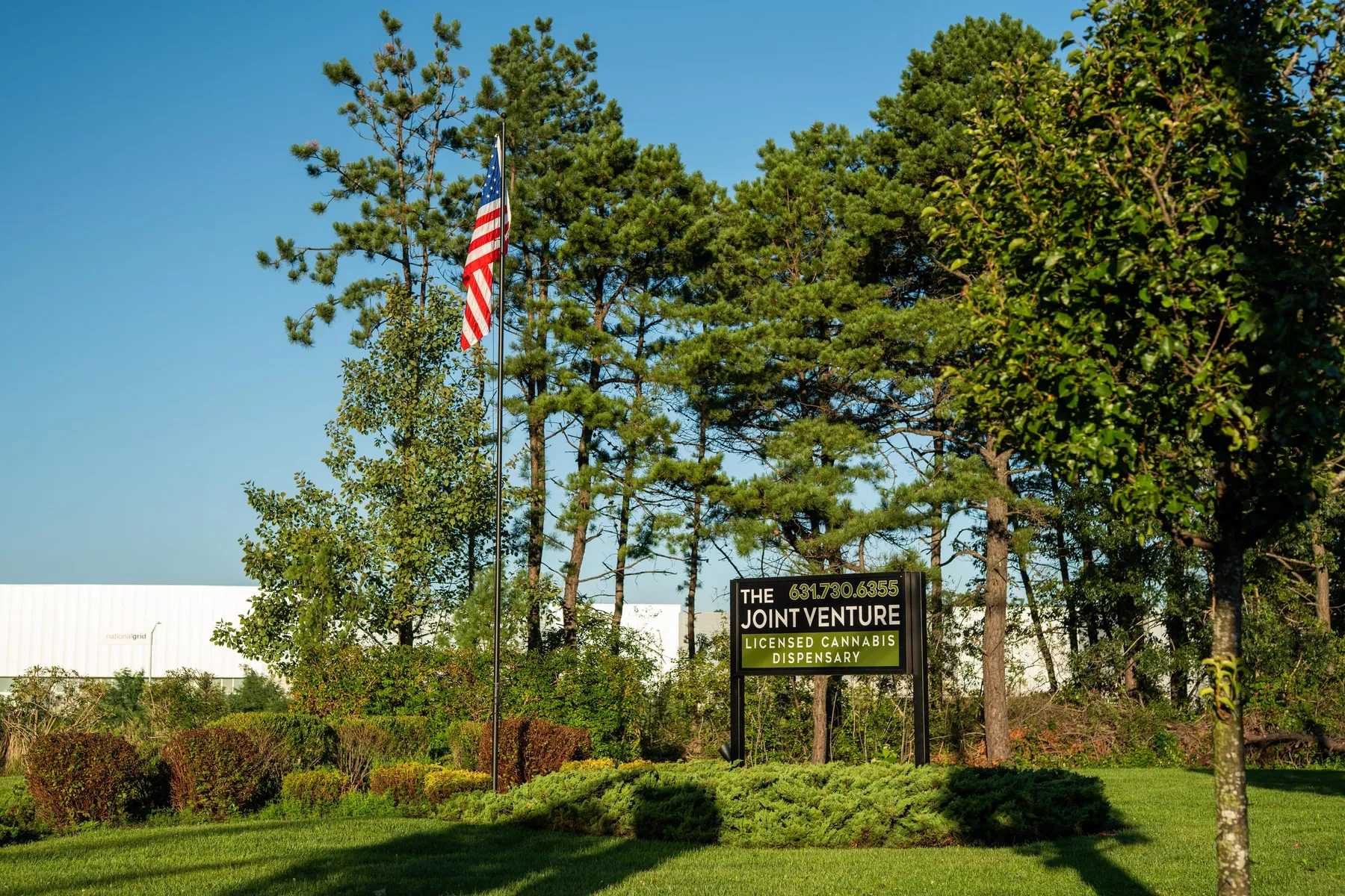 The Joint Venture's roadside sign on Munsell Road, showing the store name and phone number, beside the flagpole.
